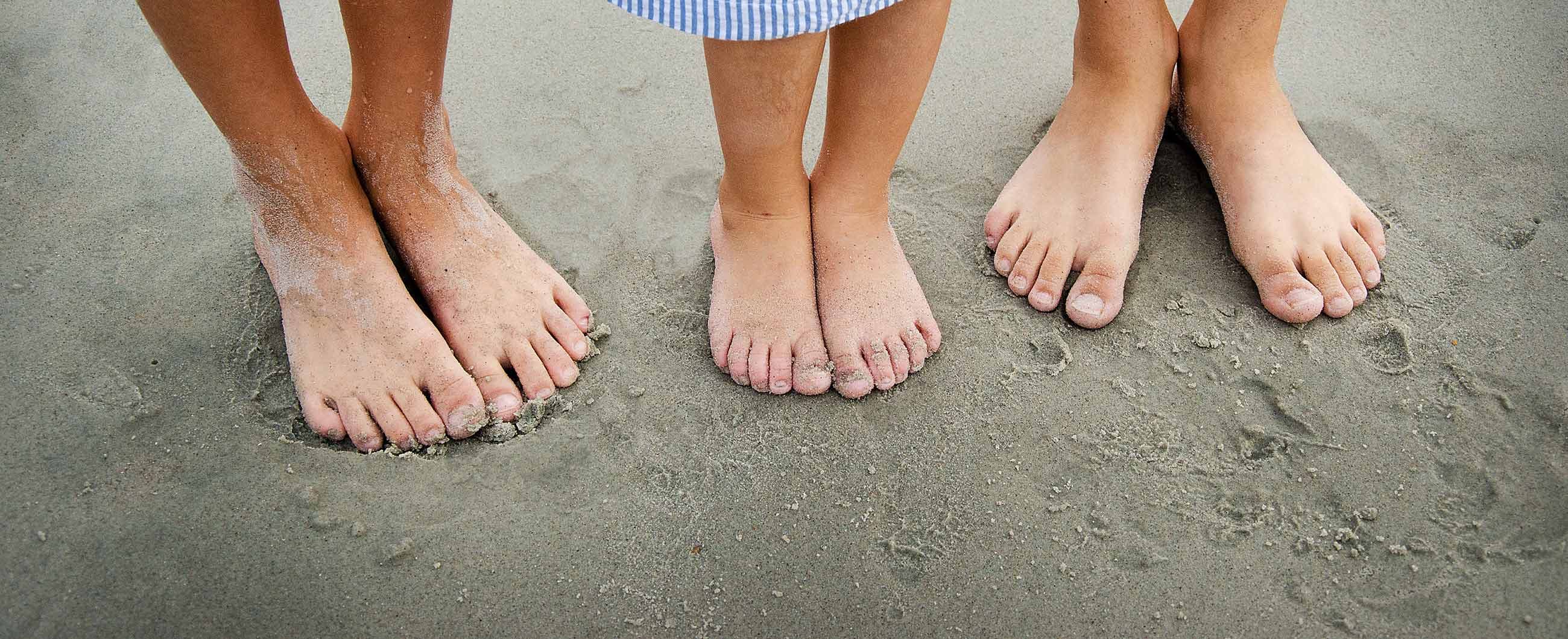 Blote voeten van een volwassene en kinderen naast elkaar in het zand